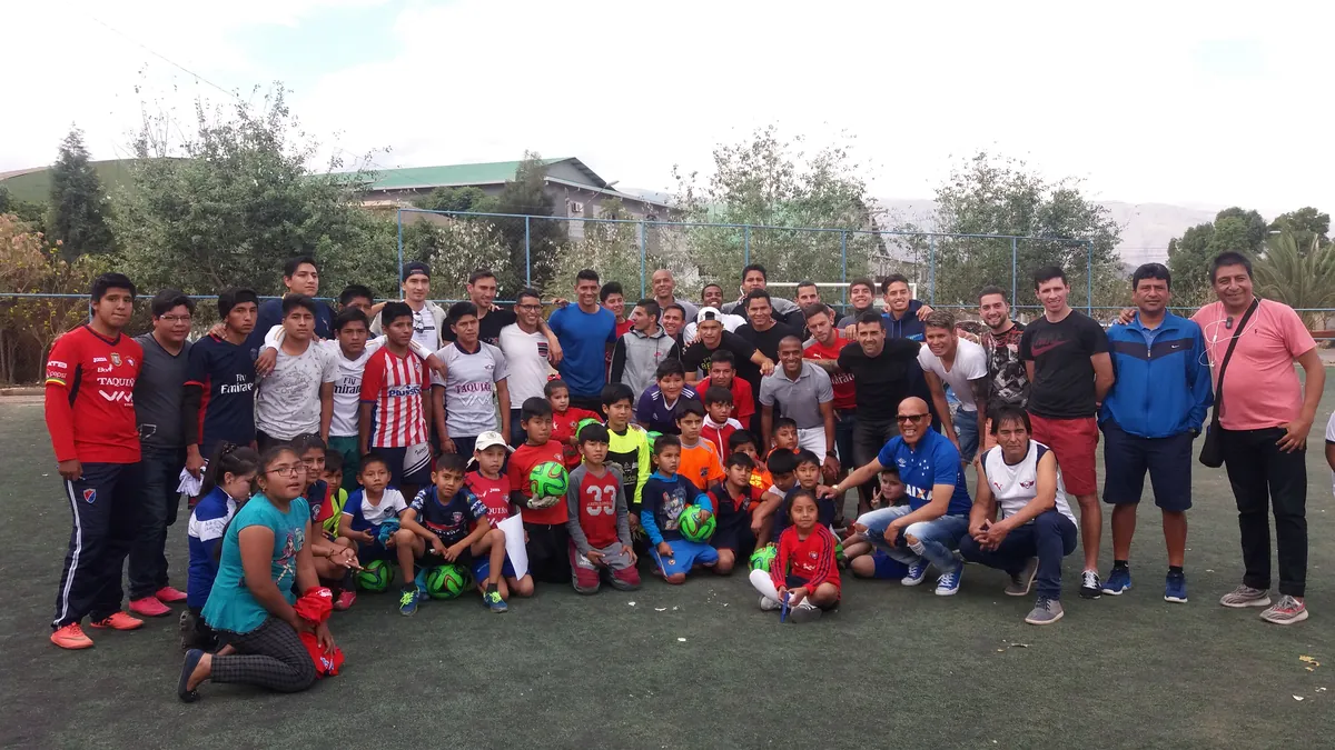 Futbolistas y niños reunidos en una cancha de fútbol, durante el trabajo con el Club Jorge Wilstermann